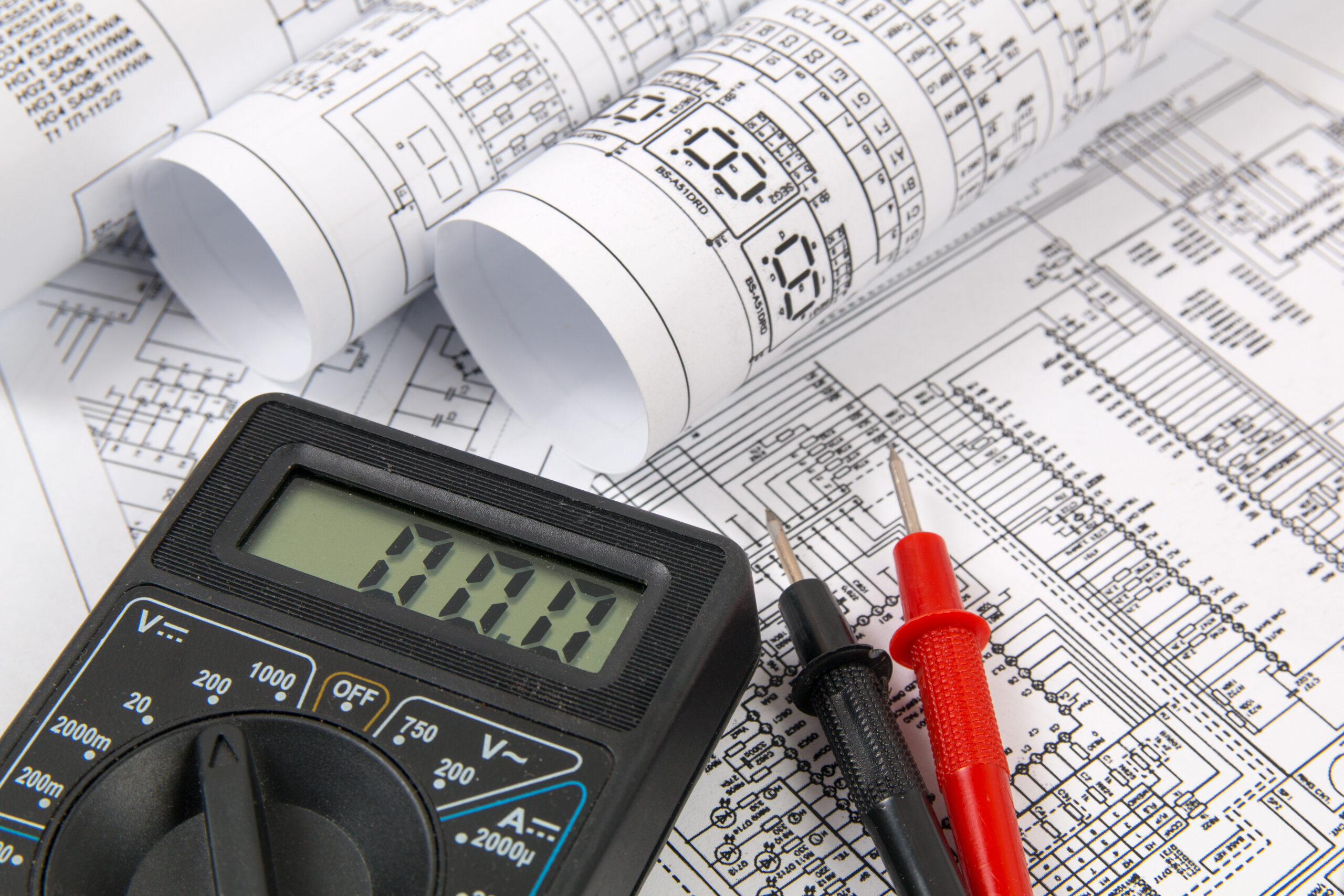 Electrical blueprints and digital multimeter used by a master electrician for planning and diagnostics.